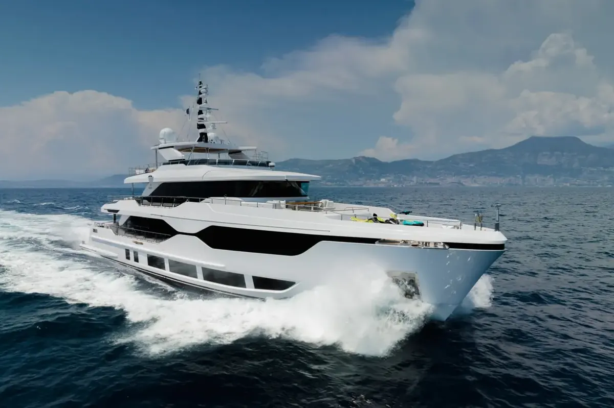 Majesty 120 superyacht running at speed with a bow wave, mountains behind